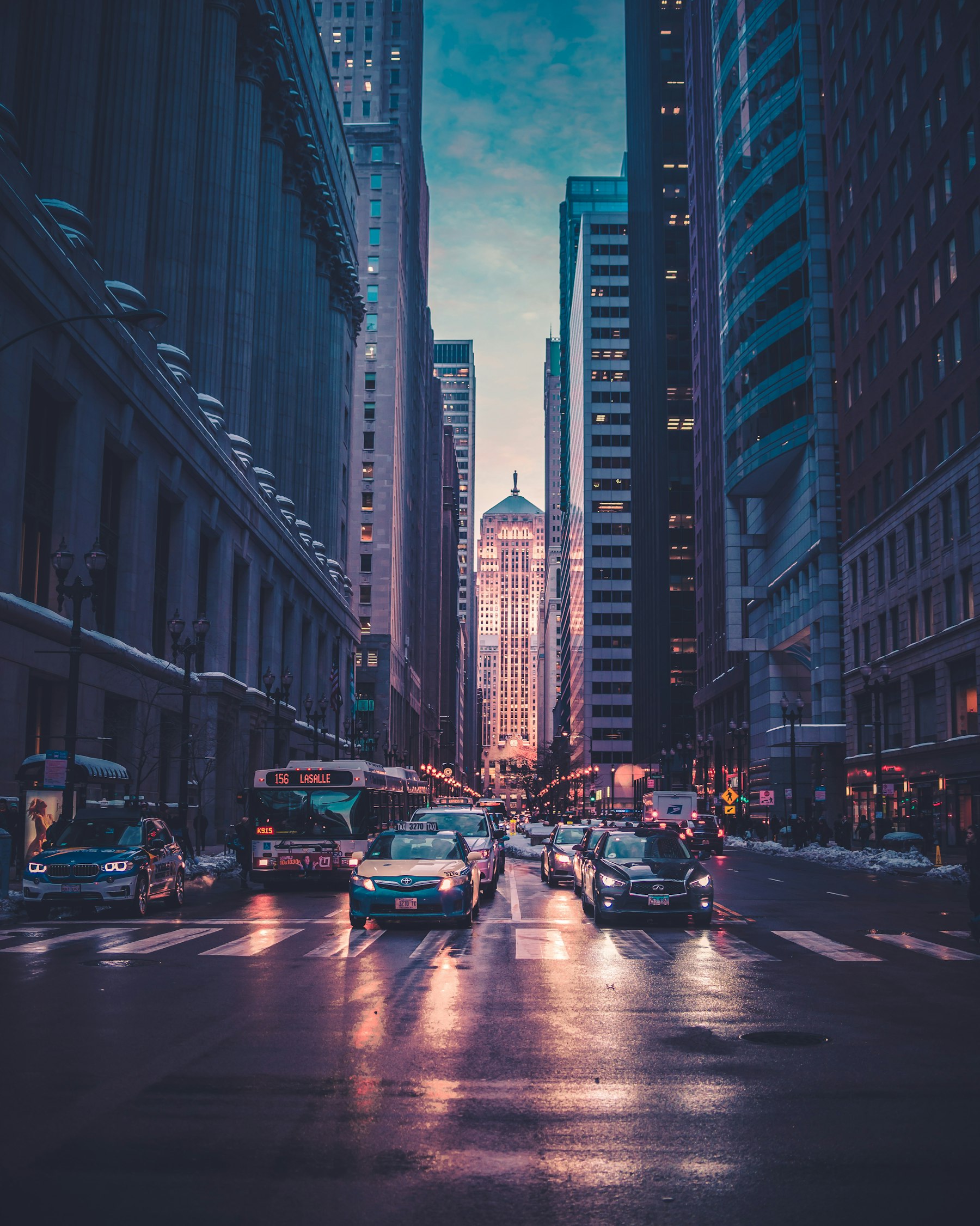 A city street at dusk with traffic and glowing skyscrapers